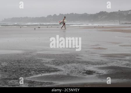 Surfeur sur la plage de Bournemouth malgré la pluie et la bruine que l'on attend dans une grande partie du pays. Banque D'Images