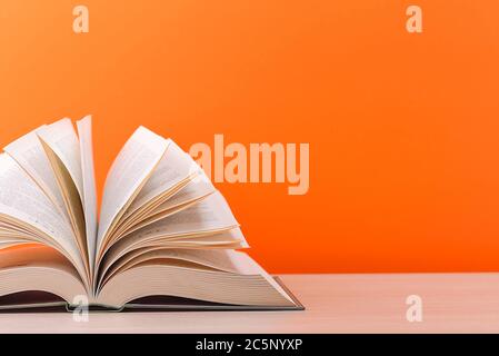 Un grand livre de couverture rigide épais repose sur une table en bois clair. Le livre est ouvert, les feuilles de la page sont défonsées, et le verso est un fond orange Banque D'Images