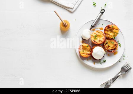 Pêches grillées au thym, au miel et à la crème glacée vanille sur fond blanc, vue du dessus, espace pour les copies. Pêches ou nectarines grillées au barbecue maison Banque D'Images