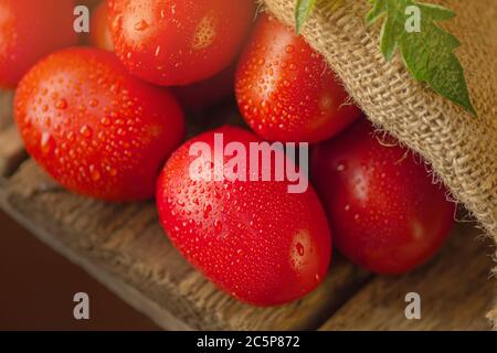 Longues tomates prune sur une table en bois. Tas de tomates fraîches dans un sac de toile sur une table en bois. Concept de produit naturel. Banque D'Images