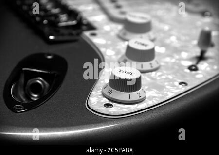 Détail noir et blanc d'une guitare électrique Fender Stratoaster montrant la prise d'entrée, les boutons de tonalité et de volume, le sélecteur, le pickguard blanc, le pont et les ramasseurs. Banque D'Images