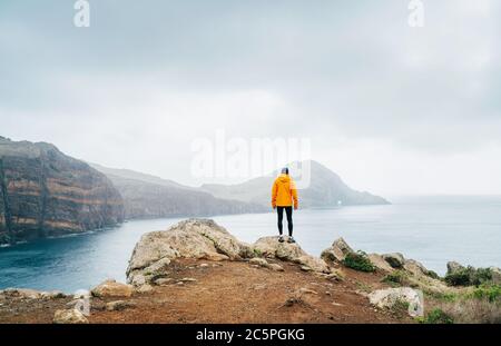 Trail runner homme habillé orange veste imperméable, collants de course et chaussures profitant de la vue sur la baie de l'Atlantique sur la péninsule de Ponta de Sao Lourenço - le e Banque D'Images