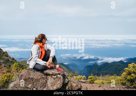 Jeune femme caucasienne vêtue de vêtements de sport, reposant sur le rocher et bénéficiant d'une vue sur les nuages depuis le mont Pico Ruivo 1861 m - le plus haut sommet sur le TH Banque D'Images