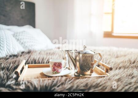 Matin 'café au lit' encore la vie. Chambre confortable avec cafetière et tasse sur la couverture de lit en sapin avec fenêtre d'arrière-plan magique. Banque D'Images