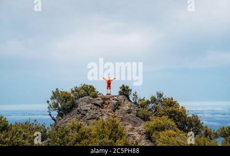 Jeune homme caucasien habillé vêtements de sport avec sac à dos rouge se levant les mains en profitant de la vue de Pico Ruivo monture 1861m - le plus haut sommet sur le TH Banque D'Images