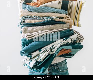 Femme portant la grande pile de linge bleu et beige dans ses mains. Image de concept de travail à domicile pour femme. Banque D'Images