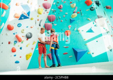 Père aidant son fils adolescent et vérifiant le harnais d'escalade près du mur d'escalade intérieur. Garçon se préparant pour une escalade. Concept de parent heureux imag Banque D'Images