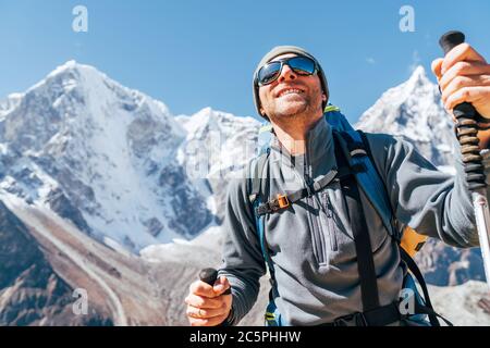 Portrait de l'homme de Hiker souriant sur Taboche 6495m et Cholatse 6440m pics fond avec des bâtons de trekking, UV protégeant des lunettes de soleil. Il appréciant la montagne Banque D'Images