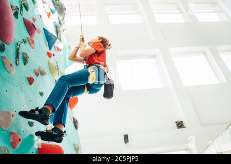 Adolescent dans le hall d'escalade intérieur. Le garçon escalade en utilisant une corde supérieure, un sac de craie et un harnais d'escalade. Concept actif de dépense de temps adolescent imag Banque D'Images