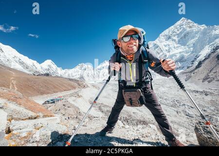 Portrait de l'homme de randonnée souriant avec le pic de Nuptse 7861 m et le fond de village de Gorak Shep avec des bâtons de trekking, UV protégeant des lunettes de soleil. Il apprécie Banque D'Images