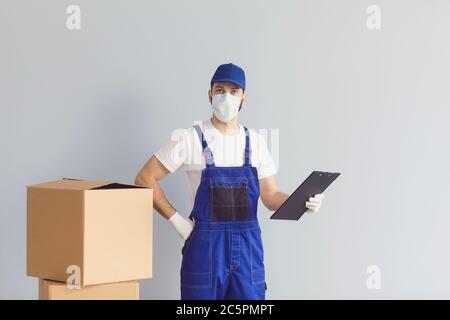 Liveur portant un masque médical avec des boîtes en carton sur fond gris. Livraison de la commande en ligne par coursier Banque D'Images