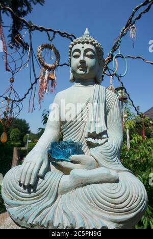 Statue de Bouddha dans notre jardin. Il y a une pierre de verre bleu sur ses genoux. Le geste de la main : toucher la Terre, qui représente le moment de l'éveil Banque D'Images