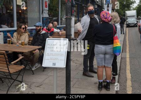 Londres 4 juillet 2020. Super samedi, bars et pubs rouvrent avec des restrictions en place, distanciation sociale, service à table, nombre limité de buveurs dans le «pub». C'est-à-dire pas de service au bar. Le service de table Portobello Road Gin Bar uniquement. Serveur parlant aux clients. Le panneau dit : « Veuillez attendre d'être assis, nous opérons un service à table seulement. Pas de paiement en espèces par carte de crédit seulement, 2020s UK HOMER SYKES Banque D'Images