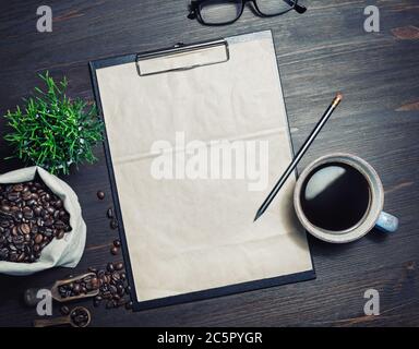 Menu et café. Presse-papiers avec papier à en-tête kraft vierge, tasse à café, plante, grains de café et crayon sur fond de bois. Vue de dessus. Pose à plat. Banque D'Images