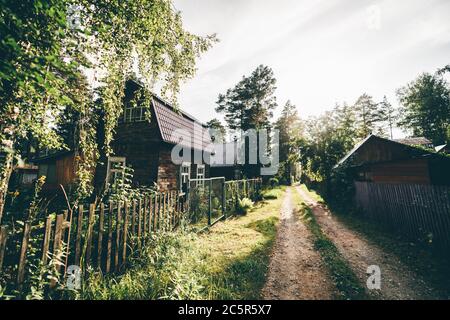 Une vue panoramique sur une rue ensoleillée de campagne d'été avec des maisons en bois sur les côtés, une ruelle étroite dans la campagne avec des dachas et une route de terre Banque D'Images