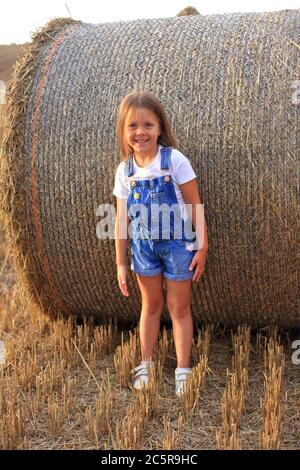 Belle petite fille se tient près d'un haystack dans un champ d'été Banque D'Images