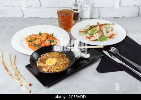 trois plats sur une table dans un restaurant, menu du café. Déjeuner d'affaires avec un bol de ramen avec poulet et œufs, salade césar fraîche et pâtes Banque D'Images