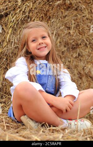 Portrait d'une petite fille sur une botte de foin en été. Banque D'Images