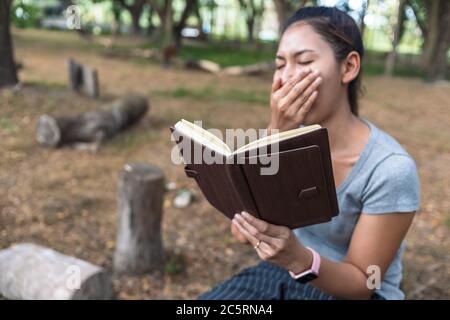 fille fatigué bâilloir s'asseoir parc et lire le livre. Banque D'Images