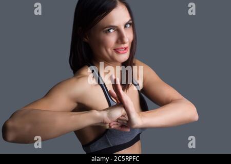 fille en pantalon de survêtement gris et haut. Montre un panneau de verrouillage, posant son poing dans la paume sur fond gris. Banque D'Images