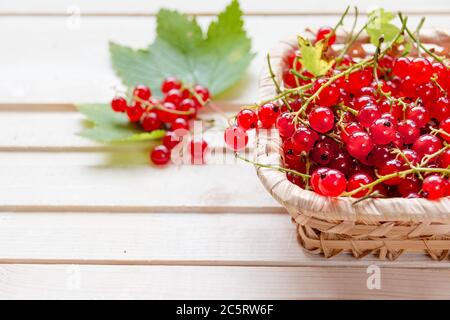Raisins de Corinthe rouges frais dans un bol sur une table en bois, mûrs Grand groseille rouge biologique dans un panier en osier.baies fraîches d'été Banque D'Images