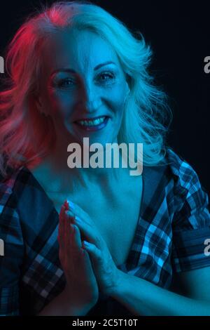 Portrait de la vieille femme dans des lumières vives colorées. Bleu et rouge, priant les mains Banque D'Images