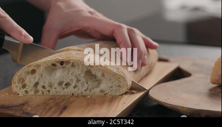 homme en tranches de ciabatta avec un couteau à pain sur une planche à olives Banque D'Images