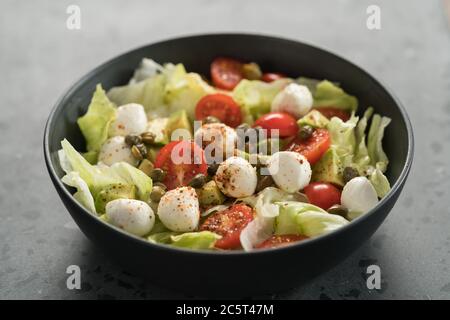 Salade avec avocat, tomates et mozzarella dans un bol noir Banque D'Images