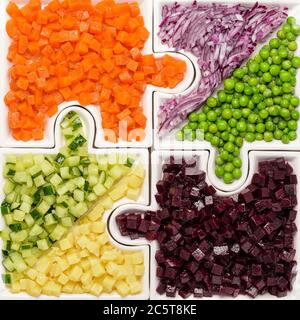 Légumes crus les carottes, les pois, les oignons, le concombre, les pommes de terre, les betteraves coupées en cubes sont sur des puzzles sous forme de puzzles et se rassemblent dans un seul grand plat Banque D'Images