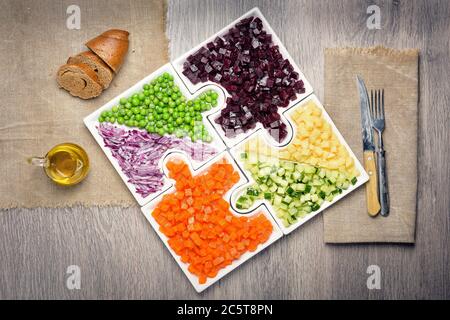 Légumes crus les carottes, les pois, les oignons, le concombre, les pommes de terre, les betteraves coupées en cubes sont sur des puzzles sous forme de puzzles et se rassemblent dans un seul grand plat Banque D'Images