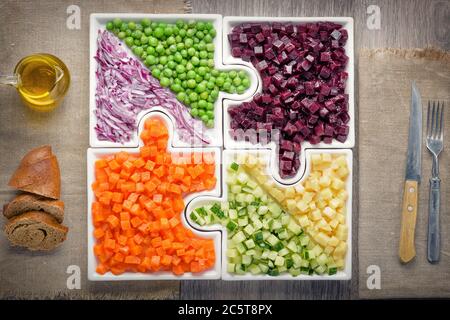 Légumes crus les carottes, les pois, les oignons, le concombre, les pommes de terre, les betteraves coupées en cubes sont sur des puzzles sous forme de puzzles et se rassemblent dans un seul grand plat Banque D'Images