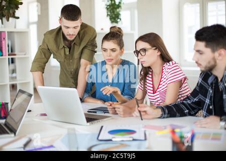 Groupe de jeunes gens d'affaires qui utilisent leur ordinateur portable ensemble. Les hommes et les femmes pensifs passent du temps au travail au bureau Banque D'Images