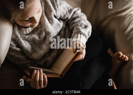 Une jeune fille blanche blonde assise sur une chaise a lu un livre Banque D'Images