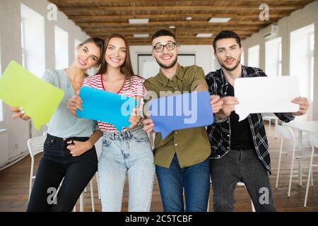 Groupe de jeunes gens joyeux montrant des journaux colorés messages icônes dans les mains regardant avec joie dans l'appareil photo tout en passant du temps au travail dans un bureau moderne Banque D'Images