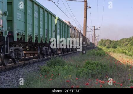 Wagons de fret dans la zone industrielle. Mouvement de train de marchandises sur les chemins de fer le long des coquelicots en fleurs. Banque D'Images