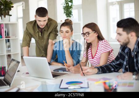 Les jeunes gens d'affaires travaillent ensemble avec soin sur un ordinateur portable. Groupe d'hommes et de femmes pensifs qui passent du temps au travail au bureau Banque D'Images