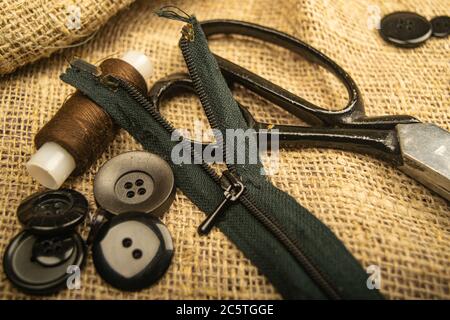 Boutons de différentes tailles, une bobine de fil, des ciseaux de tailleur, et une fermeture à glissière sur toile rugueuse-texturée. Gros plan Banque D'Images