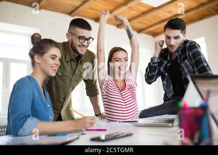 Groupe d'hommes d'affaires souriants travaillant ensemble au bureau. Les jeunes gens émotionnels passent du temps au travail avec joie Banque D'Images