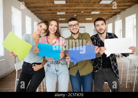 Groupe de jeunes souriants montrant des journaux colorés messages icônes dans les mains regardant joyeusement dans l'appareil photo tout en passant du temps au travail dans un bureau moderne Banque D'Images