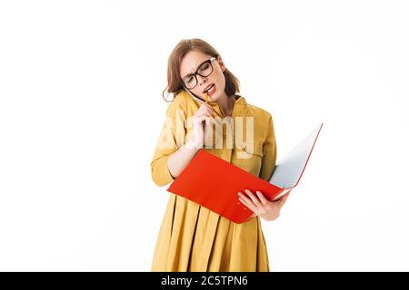 Portrait d'une jeune femme occupée à lunettes parlant sur son téléphone portable tout en regardant de côté avec dossier rouge ouvert et crayon à la main sur blanc Banque D'Images