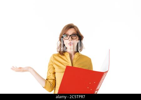 Portrait de jeune femme en lunettes debout avec dossier rouge ouvert et regardant avec étonnement dans l'appareil photo sur fond blanc isolé Banque D'Images