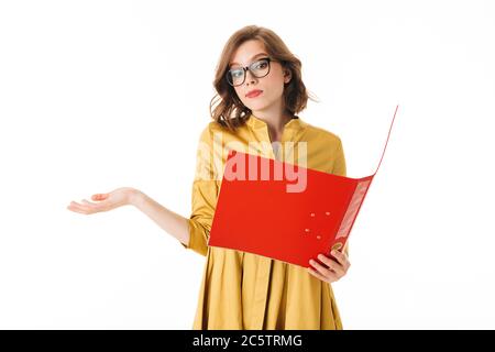 Portrait de la jolie dame en lunettes debout et regardant avec soin dans un dossier rouge ouvert sur fond blanc isolé Banque D'Images