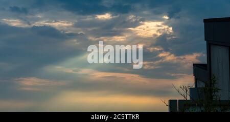 Rayons de lumière perçant à travers les nuages pendant le coucher du soleil avec des parties de toits Banque D'Images