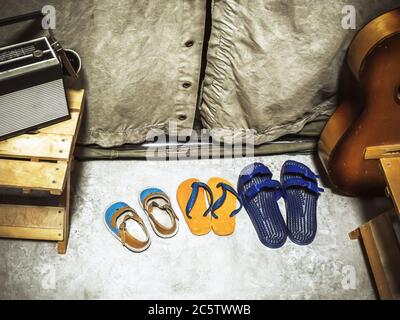 Fragment d'une ancienne tente de camping avec des chaussures debout devant elle, une guitare, un banc en bois et une radio dessus Banque D'Images