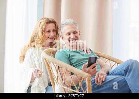 Portrait aux tons chauds d'un couple élégant et mûr regardant l'écran du smartphone tout en se relaxant à la maison, dans l'espace de copie Banque D'Images