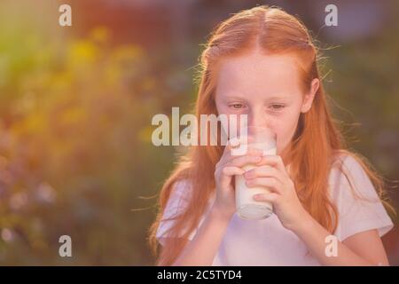 Lait sain pour bébé - Portrait d'une belle fille à tête rouge qui boit du lait frais à l'extérieur. Le lait est frais de la vache - une belle fille avec la production laitière Banque D'Images