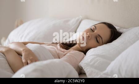 Belle jeune femme paisible dormant sous une couverture dans un lit confortable Banque D'Images