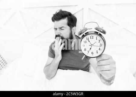 Heure de réveil. Habitudes saines. Début d'une journée extraordinaire. Réveillez-vous tôt tous les matins. Les avantages pour la santé de la hausse précoce. Se réveiller tôt donne plus de temps. Hipster barbu homme au lit avec réveil. Banque D'Images