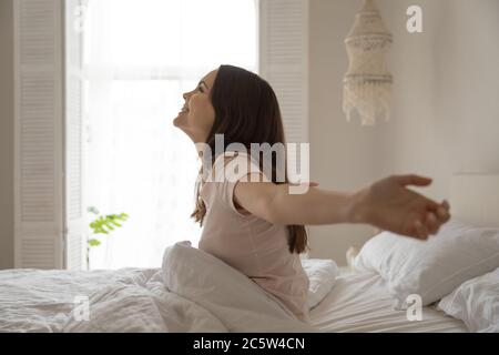 Souriante belle femme assise dans le lit, s'étirant après le réveil Banque D'Images