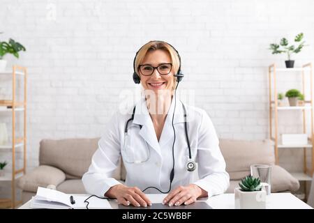 Médecin de famille consulte à distance. Un médecin souriant dans un casque se trouve à table avec un ordinateur portable Banque D'Images